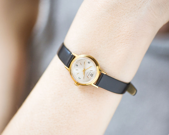 The tiny gold-plated watch on the woman’s wrist. The dial of the watch is with Arabic numerals, minimalist style, classic watch tiny little for every occasion. A piece of pre-owned vintage jewelry. You can make a better choice for the Planet.