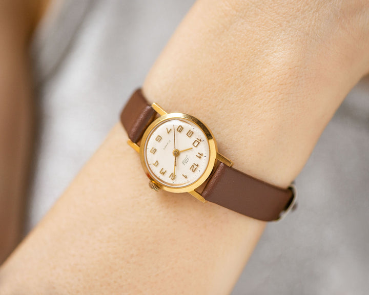 The tiny gold-plated watch on the woman’s wrist. The dial of the watch is with Arabic numerals, minimalist style, classic watch tiny little for every occasion. A piece of pre-owned vintage jewelry. You can make a better choice for the Planet.