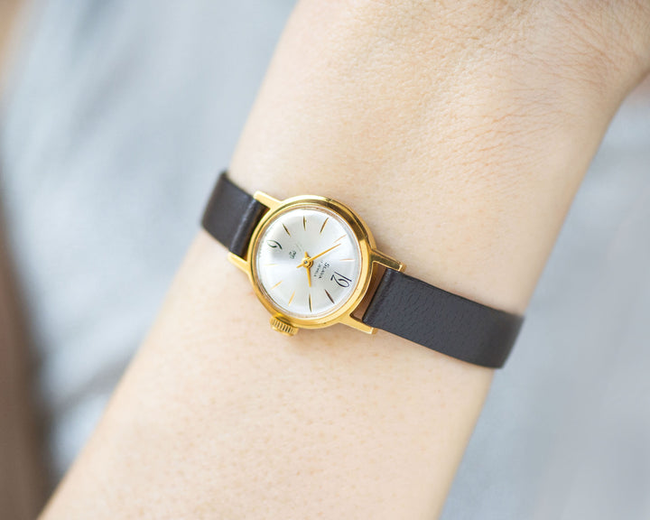 The tiny gold-plated watch on the woman’s wrist. The dial of the watch is with Arabic numerals, minimalist style, classic watch tiny little for every occasion. A piece of pre-owned vintage jewelry. You can make a better choice for the Planet.