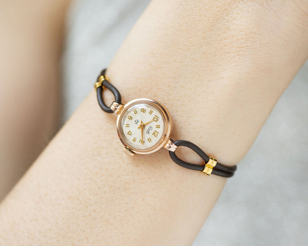 The tiny solid gold watch on the woman’s wrist. The dial of the watch is with Arabic numerals, minimalist style, classic watch tiny little for every occasion. A piece of pre-owned vintage jewelry. You can make a better choice for the Planet.