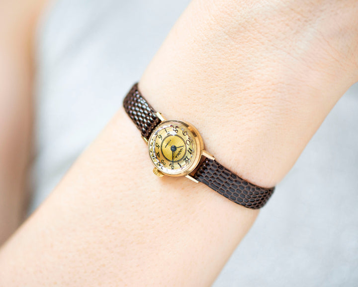 The tiny gold-plated watch on the woman’s wrist. The dial of the watch is with Arabic numerals, minimalist style, classic watch tiny little for every occasion. A piece of pre-owned vintage jewelry. You can make a better choice for the Planet.