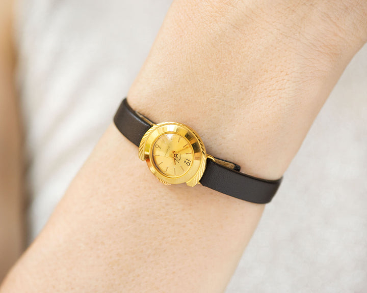 Limited edition tiny gold-plated watch on the woman’s wrist. The dial of the watch is yellow with Arabic numerals, swirl case, a classic watch tiny little for every occasion. Never been used vintage jewelry.