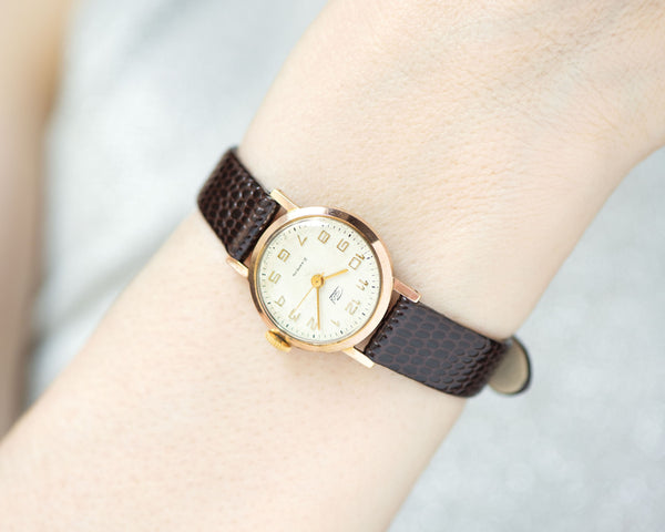 The tiny gold-plated watch on the woman’s wrist. The dial of the watch is with Arabic numerals, minimalist style, classic watch tiny little for every occasion. A piece of pre-owned vintage jewelry. You can make a better choice for the Planet.