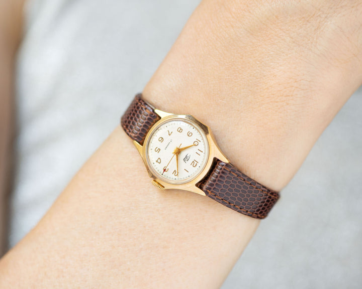 The tiny gold-plated watch on the woman’s wrist. The dial of the watch is with Arabic numerals, minimalist style, classic watch tiny little for every occasion. A piece of pre-owned vintage jewelry. You can make a better choice for the Planet.